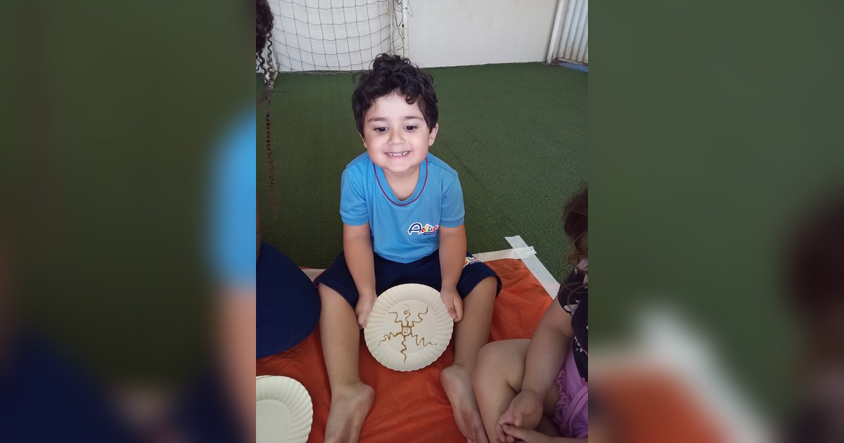 Um menino de cabelo encaracolado e escuro, vestindo camiseta azul com o logo 