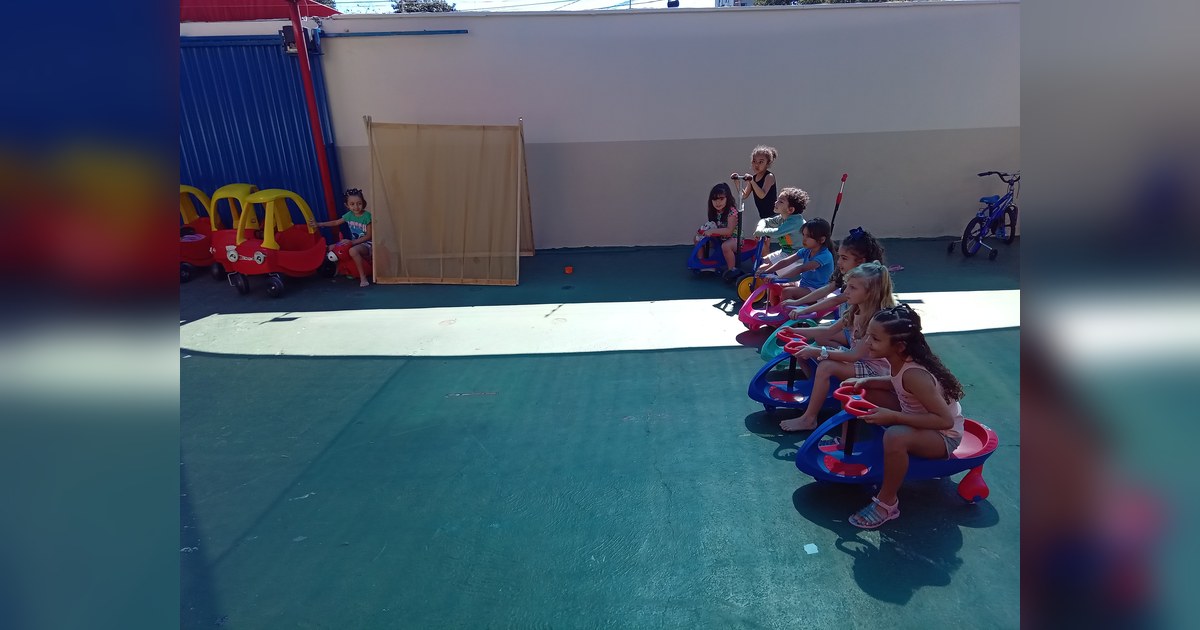Nove crianças de idade pré-escolar, de diversas etnias, estão em uma área externa. Tema - parquinho escola infantil na Escola Aclive, Setor Vila Rosa, Goiânia, Goiás.