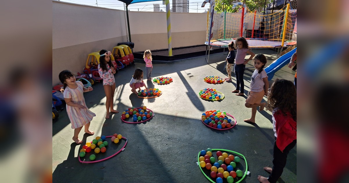 Nove meninas, com idade estimada entre 3 e 7 anos, brincam descalças em uma área externa de recreação. Tema - desenvolvimento infantil na Escola Aclive, Setor Vila Rosa, Goiânia, Goiás.