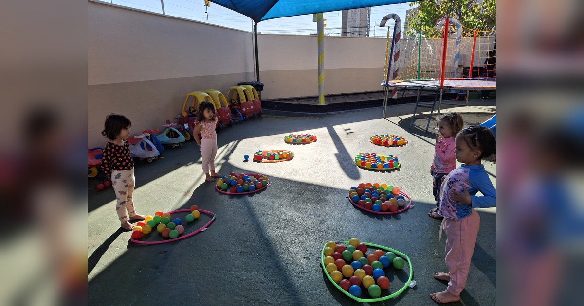 Cinco crianças pequenas, aparentemente meninas, estão em um pátio externo de escola infantil. Tema - escola infantil período integral na Escola Aclive, Setor Vila Rosa, Goiânia, Goiás.